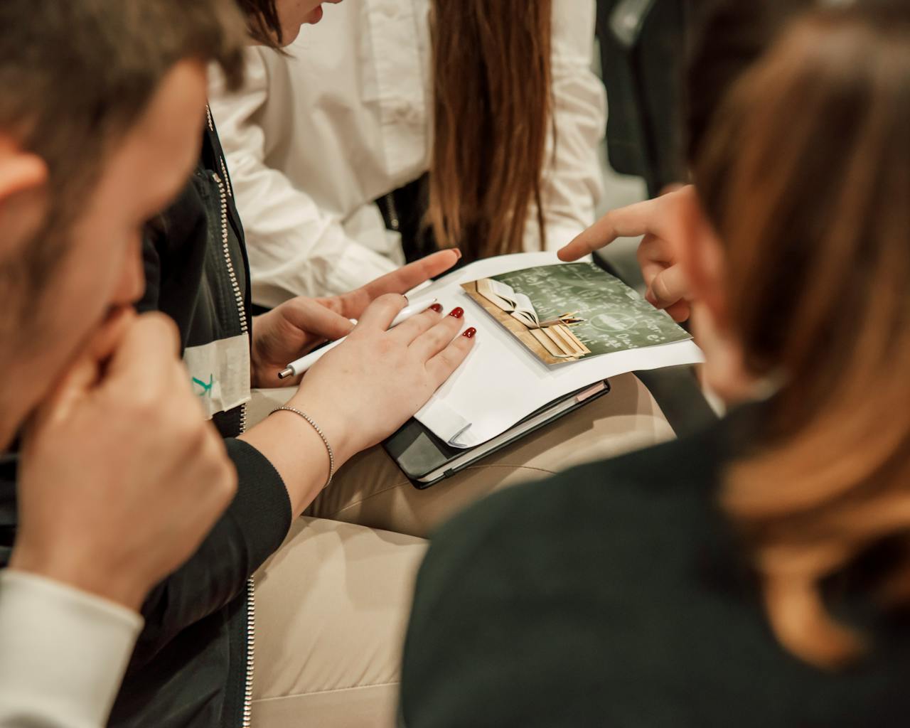 contact-img Close-up of people engaged in a group study session, sharing ideas with a book.